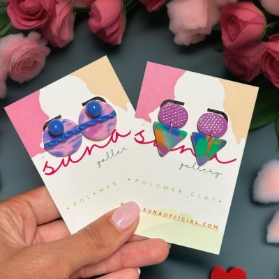 Dois pares de brincos de polymer clay em cartão com fundo de flores rosas e coração vermelho