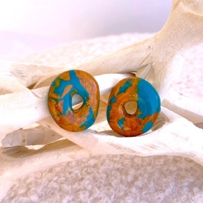 Brincos redondos de resina marrom e azul sobre estrutura branca.