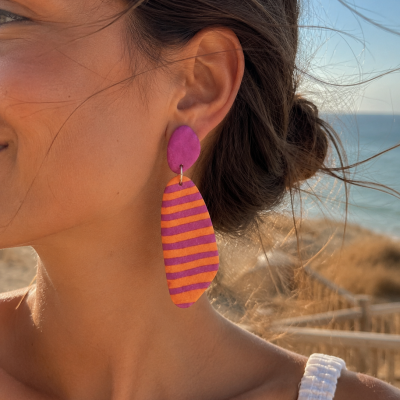 Brinco pendente rosa e laranja usado por mulher junto ao mar