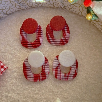 Brincos geométricos com padrões vermelhos e brancos dispostos em superfície macia clara