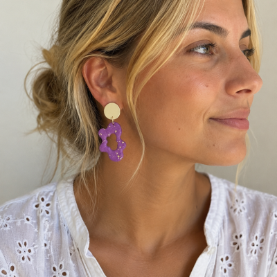 Brincos com disco dourado e flor roxa com detalhes dourados em mulher loira com camisa branca bordada