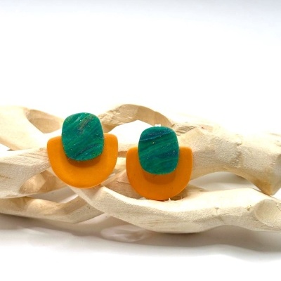Par de brincos com base laranja e topo verde textura marmoreada em estrutura de madeira clara entrelaçada