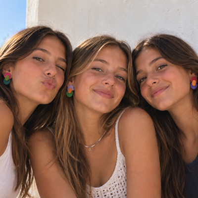 Três jovens com brincos geométricos coloridos e roupa casual ao ar livre