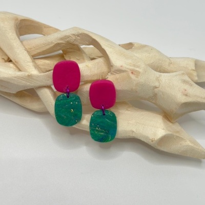 Brincos de resina rosa e verde sobre objeto de madeira claro