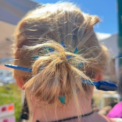 Pessoa com cabelo loiro preso em coque com ganchos de cabelo azuis e verdes ao ar livre