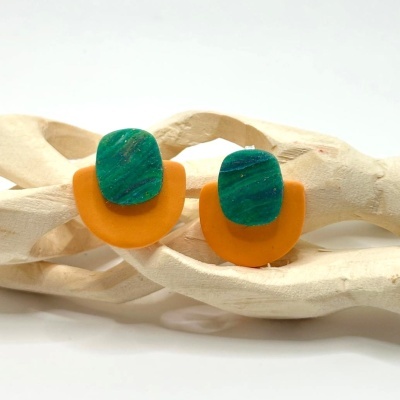 Brincos laranja e verde com design moderno sobre fundo branco e peça decorativa de madeira clara