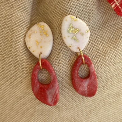 Brincos branco e vermelho com manchas douradas e recorte oval sobre tecido bege