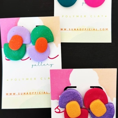 Brincos de polymer clay coloridos em cartões com texto WWW.SUNAOFFICIAL.COM.