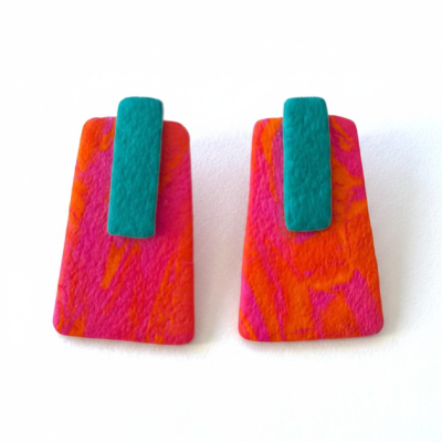 Brincos retangulares laranja e rosa com detalhes azul-turquesa numa superfície branca