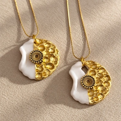 Dois colares com pendentes redondos branco e dourado sobre fundo bege.