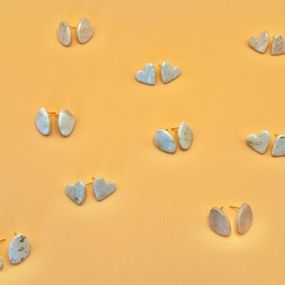 Brincos em formato de corações e oval de resina branca com detalhes dourados sobre fundo laranja