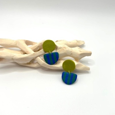 Brincos verde oliva e azul com riscas sobre ramo de madeira branca