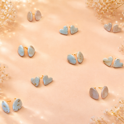 Brincos pequenos ovais e em forma de coração em tons pastel sobre tecido cor de pêssego