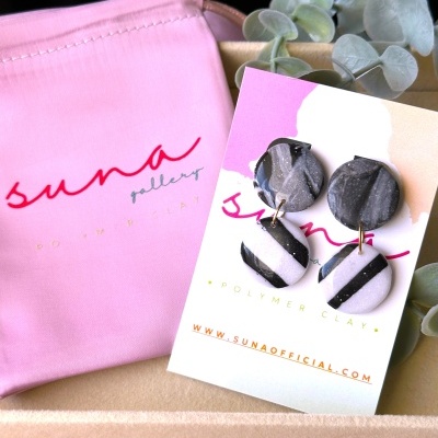 Brincos redondos em polymer clay preto, branco e cinza com padrão de riscas e mármore em cartão e saco rosa suna gallery