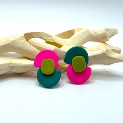 Par de brincos coloridos em cerâmica sobre superfície branca com decoração de madeira clara.