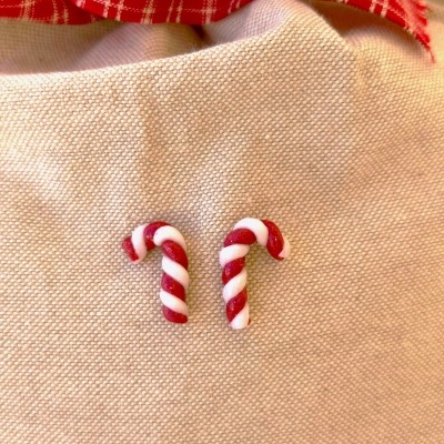 Dois pequenos pauzinhos de doces em forma de bengala vermelhos e brancos sobre tecido bege e pano vermelho xadrez ao fundo.