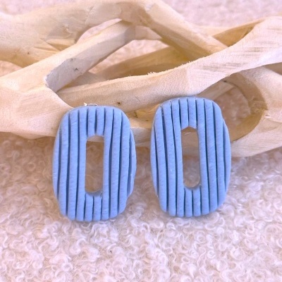 Brincos ovais azuis com linhas verticais em fundo branco felpudo e madeira clara