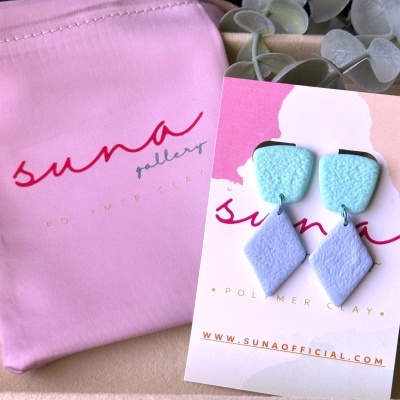 Brincos geométricos azuis claros em cartão de marca e saco rosa claro