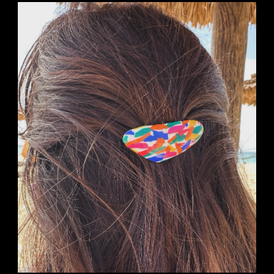 Presilha de cabelo multicolorida em cabelo castanho com fundo de palha e céu