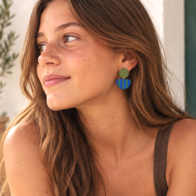 Brincos verde e azul com riscas usados por mulher com cabelo castanho ondulado e pele com sardas