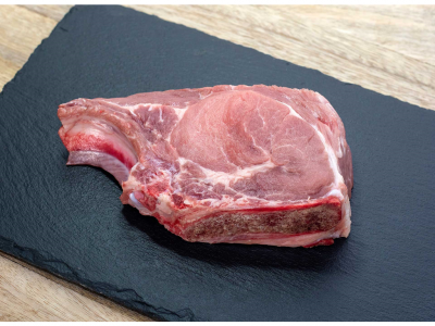 Bife cru com osso sobre placa preta de ardósia em mesa de madeira