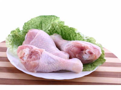 Três coxas de frango cruas com alface numa travessa branca sobre madeira