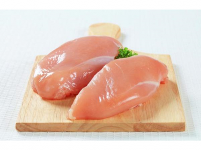 Dois peitos de frango crus num tabuleiro de madeira claro com salsa.