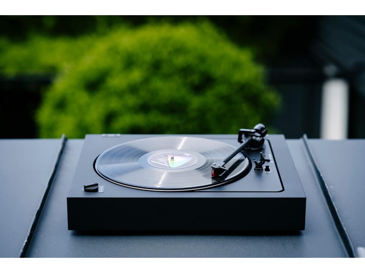 A2 - Gira-Discos Automático Gira-discos preto com disco de vinil transparente numa mesa preta com fundo verde