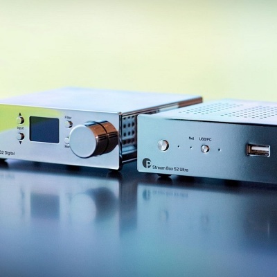 Dois dispositivos eletrônicos prateados com botões, display e porta USB sobre superfície refletora