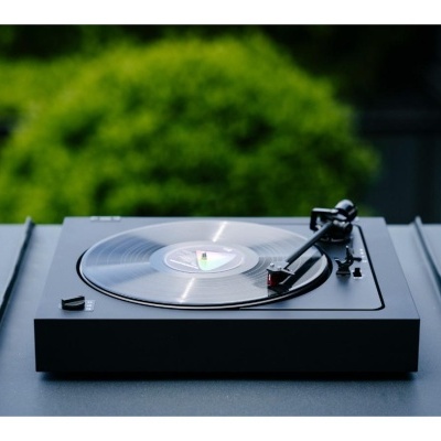 Gira-discos preto com disco de vinil transparente numa mesa preta com fundo verde