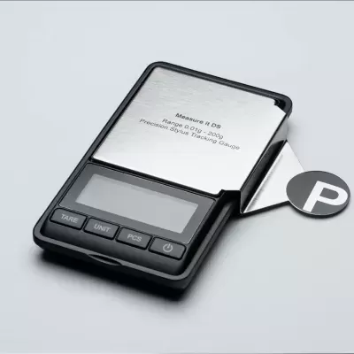 Balança digital prateada e preta com ecrã e botões, sobre fundo cinzento