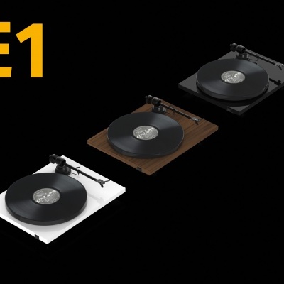 Três gira-discos E1 em branco, madeira castanho e preto com discos vinil em fundo preto