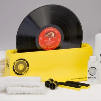 Conjunto de limpeza para discos vinil com recipiente amarelo, garrafas de líquido, escovas e disco vinil.