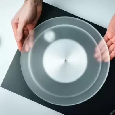 Prato redondo transparente fosco segurado por duas mãos sobre fundo preto e branco