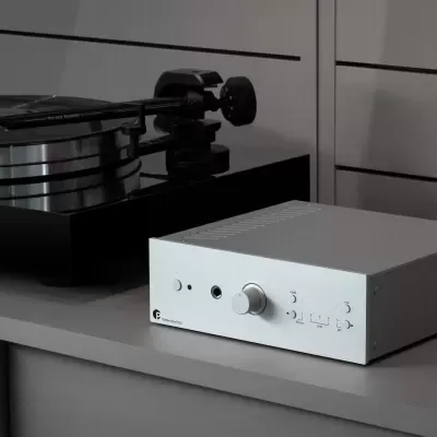 Leitor de vinil preto com base prateada e amplificador branco sobre superfície cinzenta