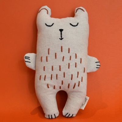 Boneco de tecido em forma de animal bege com bordados pretos e castanhos