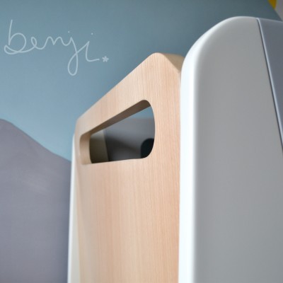 Móvel em madeira clara e branca com recorte para pega, parede azul com desenho de montanhas e escrito benji