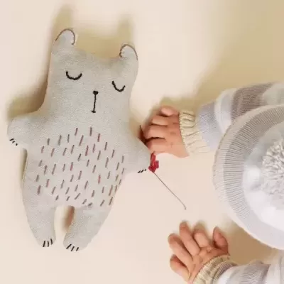 Urso de peluche cinzento com bebé vestido de roupa clara e gorro branco