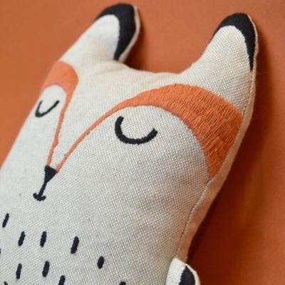 Almofada decorativa em forma de raposa tons creme, laranja e preto com padrão e olhos fechados