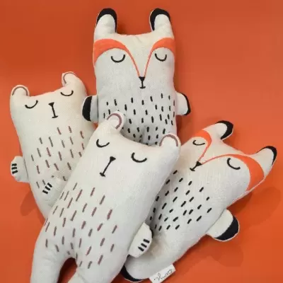Peluches de animais branco com detalhes castanhos, pretos e laranja sobre fundo laranja