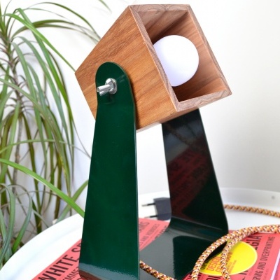 Lâmpada de secretária com estrutura verde e corpo de madeira em mesa branca com revistas