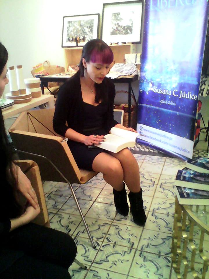 Mulher sentada a ler livro com banner azul ao fundo e cadeira de madeira