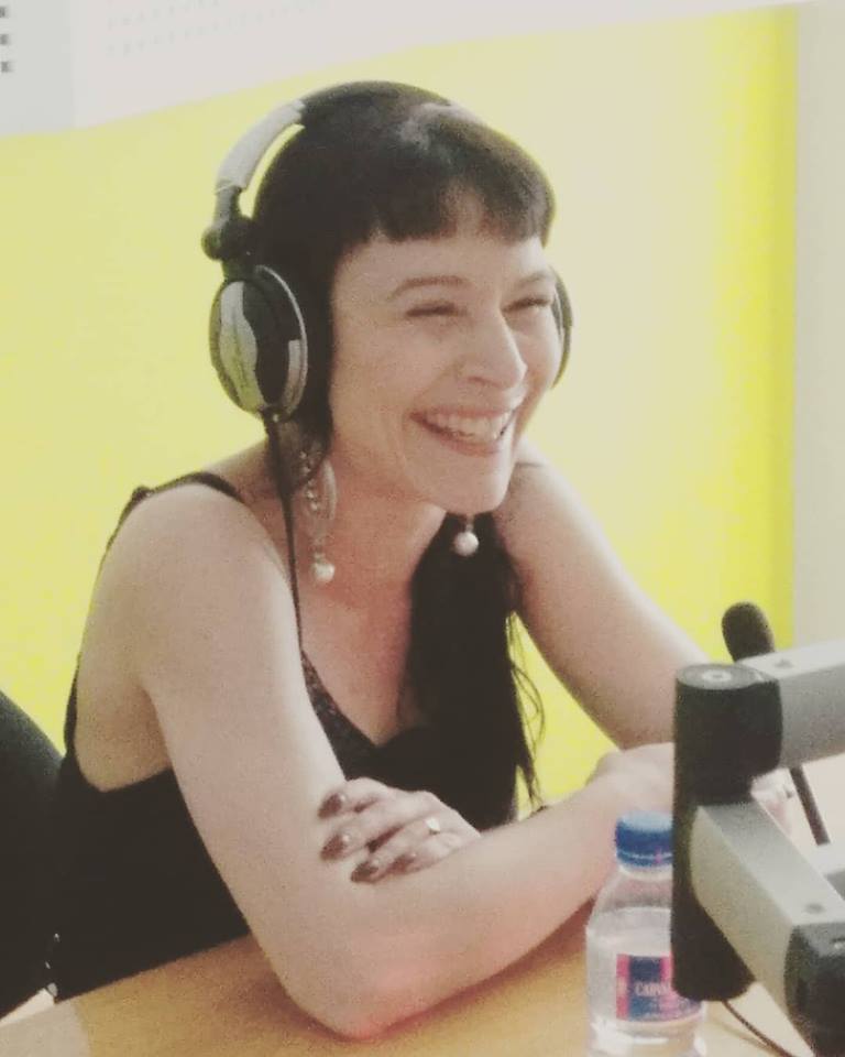 Mulher com auscultadores e vestido preto num estúdio com microfone e garrafa de água