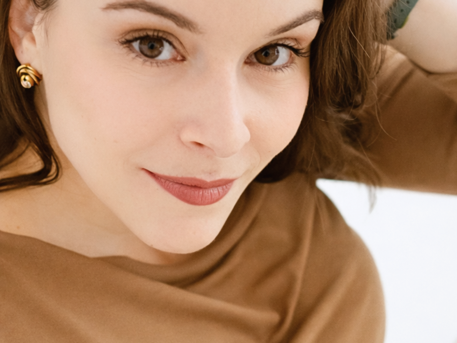 Brincos dourados com detalhe transparente em mulher de camisola castanha