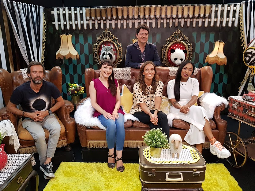 Grupo de pessoas sentadas em sofá de couro castanho em sala decorada com máscaras e luminárias vintage