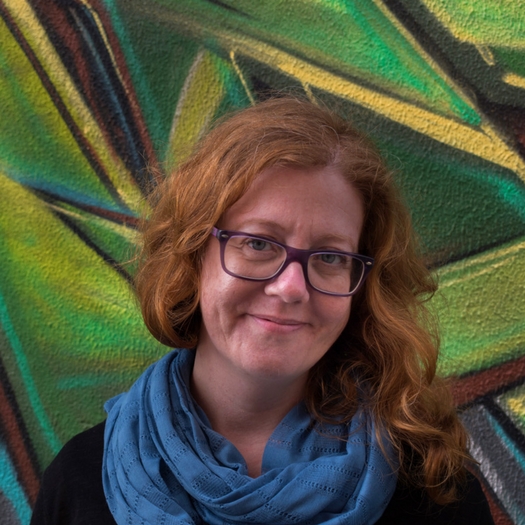 Entrevista para a Tripper por Sandra Henriques Gajjar Pessoa com lenço azul e óculos roxos diante de mural colorido