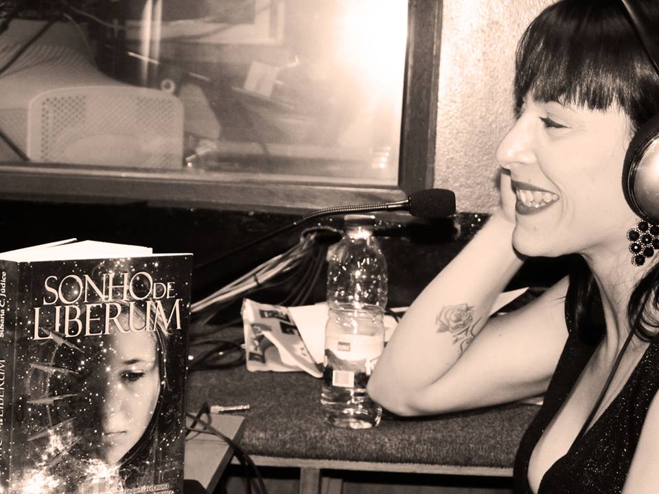 Mulher com auscultadores ao lado de livro 'SONHO DE LIBERUM' e garrafa de água na mesa