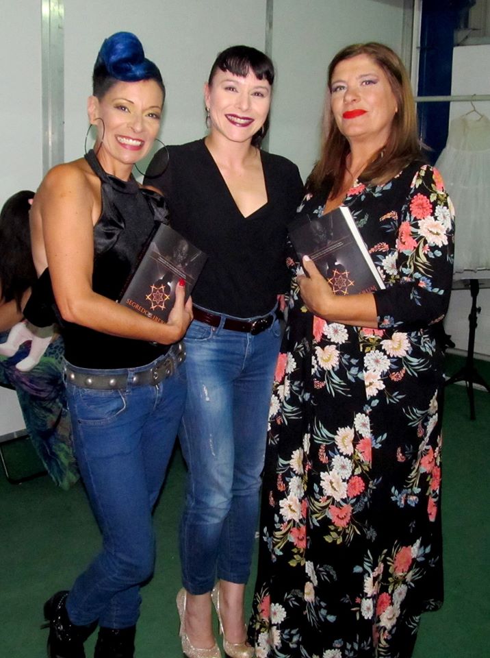 Três mulheres num ambiente interior com livros e roupa colorida