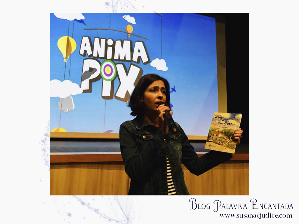 Mulher a falar num microfone e a mostrar um livro em evento ANIMA PIX