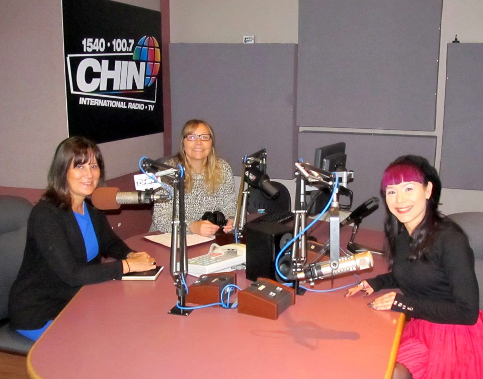 Três mulheres em estúdio de rádio com microfones e placa CHIN ao fundo